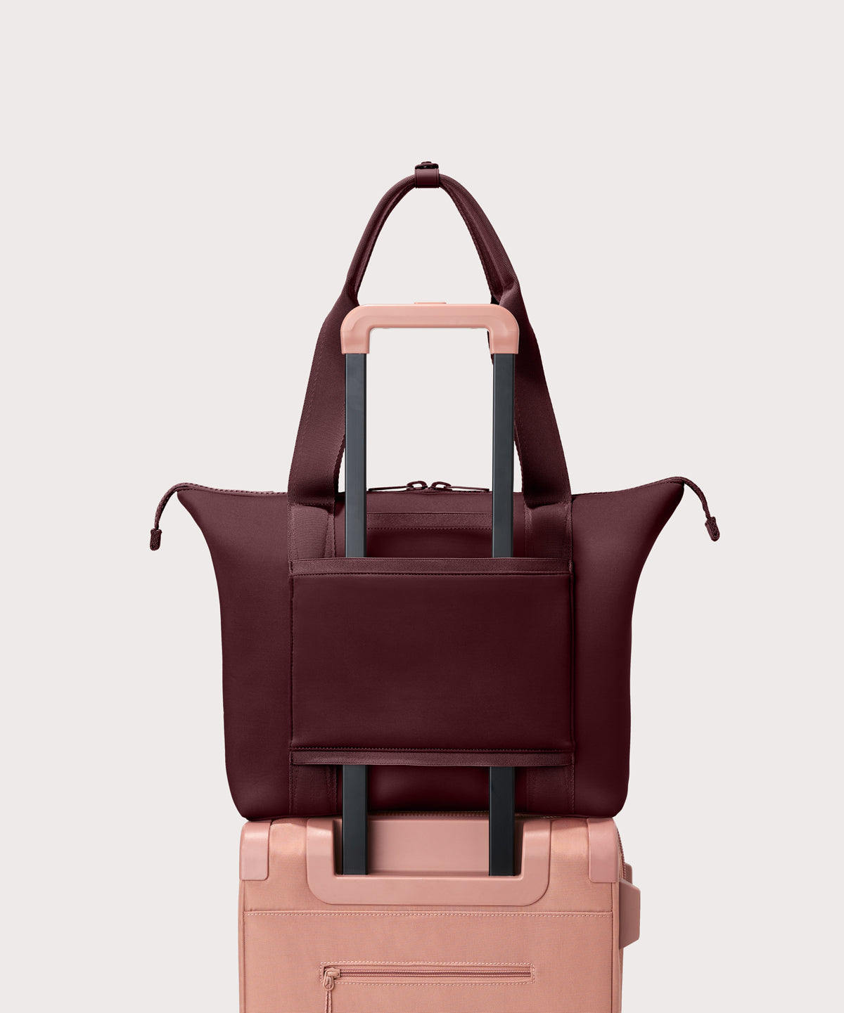 Tote bag in a deep brown with purple undertones reminiscent of maroon seen from the back view on suitcase.
