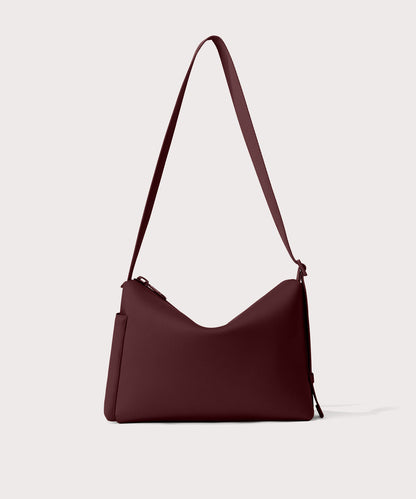 Shoulder bag in a fiery, deep brown with purple undertones reminiscent of maroon seen from the back view showing phone pocket.
