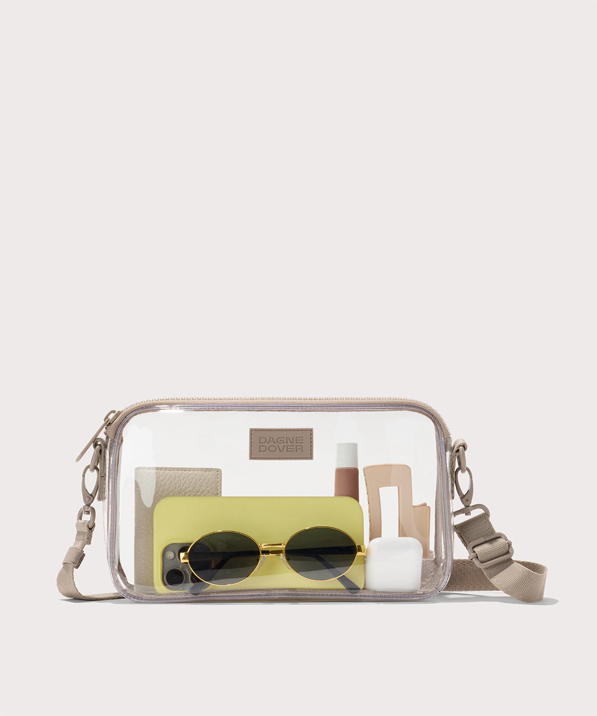 Clear crossbody bag with sunglasses, phone, and other accessories with a beige strap. Stadium compliant.