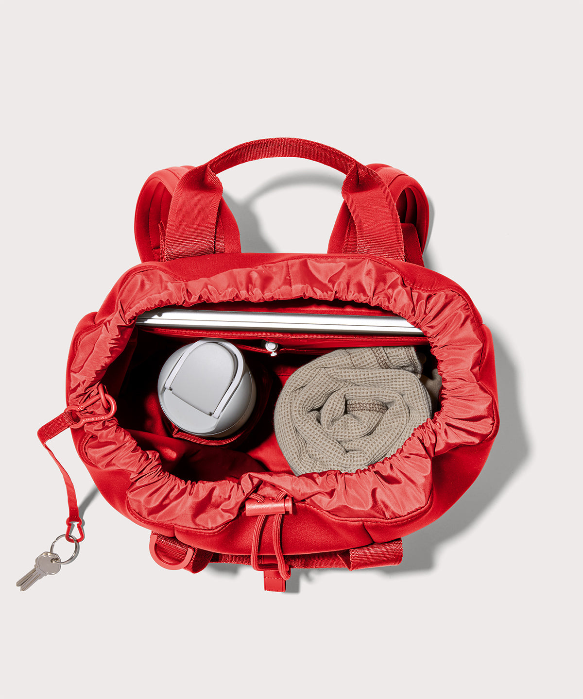 Dagne Dover Rhys Backpack in a fiery, saturated red leaning toward orange unzipped, showing the interior pockets and drawstring closure.