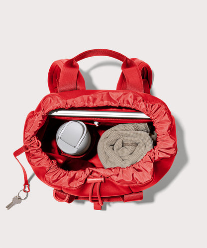 Dagne Dover Rhys Backpack in a fiery, saturated red leaning toward orange unzipped, showing the interior pockets and drawstring closure.