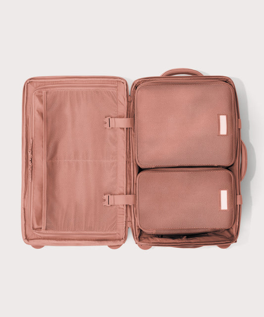 Top down of Seattle carry-on rolling luggage 23.5” in warm dust pink with interior divider zipped and packing cubes packed into the right side.